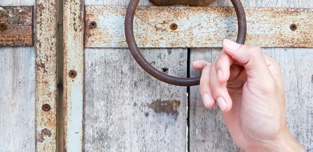 Close up hand holding rusty door knocker on old wooden door background - Object, Part of body, Vintage style and Decorated conceptの写真素材