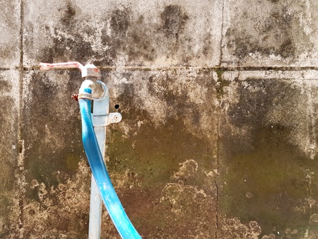 Close up old stainless steel Faucets and blue water rubber hoses on dirty rough cement wall with...