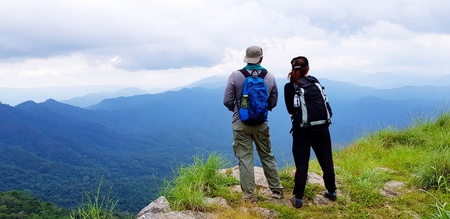 Couple hiker with backpack standing on the top of mountain with blue sky, white cloud and mist at...