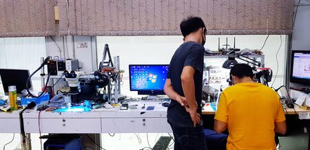 Bangkok, Thailand - April 2, 2019: Two people fixing or checking mobile phone or electronic device with tester or tool in laboratory with copy space - Technology, Maintenance or Technical conceptのeditorial素材