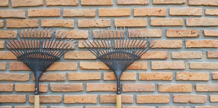 Two black rake hanging or leaning against on brick wall with right copy space - Agriculture tool or...