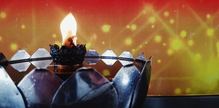 Close up flame, fire or candle light burning in oil lamp or lantern for worship or pay respect Buddha image and monk with red/yellow background and copy space at Thai temple- Art and Religion conceptの写真素材