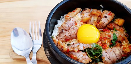 Close up Stir fried Thai basil with crayfish and yolk egg in hot black bowl with stainless steel...