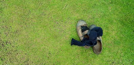 Top view of old shoes and black socks putting on green grass field background with left copy space -...