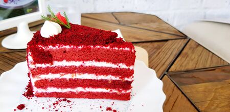 Piece of Raspberry red velvet cake with Lemon cream cheese frosting on white plate putting on wooden...