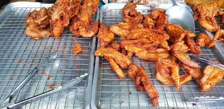 Many fried chicken and belly pork with stainless tongs and oil for frying on stainless steel grille for sale on street food market - Fat food and Unhealthy eating life style conceptの写真素材