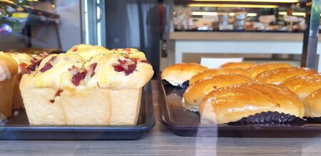 Close up sweet soft bread in black tray on wooden shelf for sale inside bakery shop with blurred...