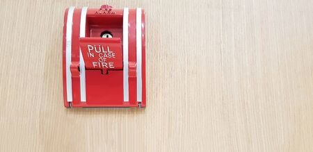 Fire alarm switch box for pull in case of fire isolated on light brown wooden background with right...