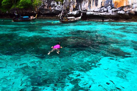 Asian man or Tourism in purple or violet life jacket with diving mask is snorkeling among many Indo-Pacific sergeant fish on Andaman Sea, Krabi, Thailand- Sport, Activity and Beauty of Nature conceptの写真素材