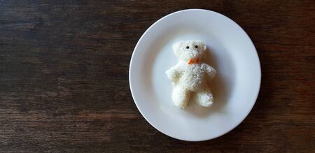 Top view cute teddy bear shape made from white rice on dish or plate on brown wooden table and copy space on left at restaurant. Create, design and make food tasty for kids or customers to eat.の写真素材