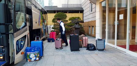 Japan- February 23, 2019: Bellboy or driver wearing mask for protection dust or virus and loading bag and luggage into the vehicle or bus to prepare for the trip. Service mind and Trip or Tour conceptのeditorial素材