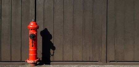 Red fire hydrant installed on sidewalk, street or road with shadow on black wooden background with...