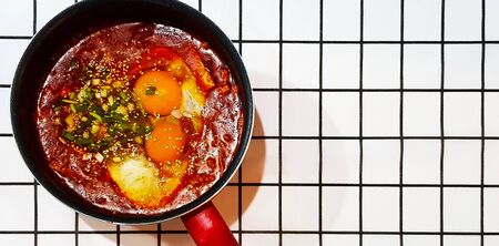Top view of hot soft tofu stew Korean style with egg, kimchi, Kochu sauce, pork sliced topping with spring onion slices and sesame in pot on table cloth background with copy space on right.の写真素材