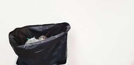 Black plastic bag containing full garbage isolated on white wall background with copy space on...