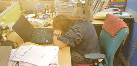 Asian woman staff sitting and sleeping on wooden table during work near black notebook, bag with orange light and document background at office -Lazy employee conceptの写真素材