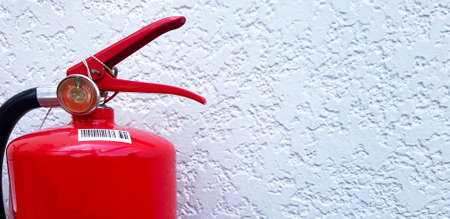 Red fire extinguisher on white rough concrete wall with copy space on right. Close up an object, Protective tool for suppressing fire.の写真素材