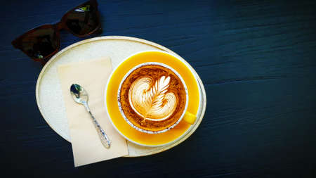 Top view of cup of art cappuccino or latte coffee putting in tray with tea spoon, napkin and brown...