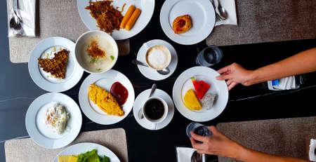 Top view of Breakfast in morning with hands of people serving Fresh fruit, poached egg, waffle,...