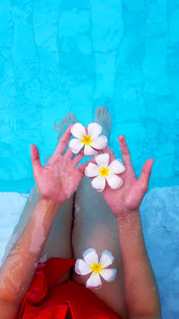 Top view of two woman's hands holding white flower or plumeria on water or swimming pool background...