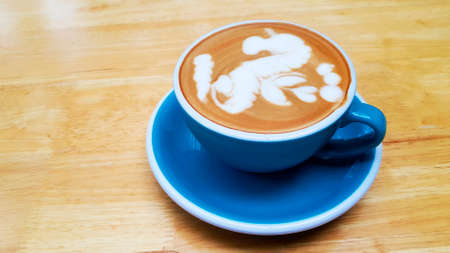 Close up blue cup of art cappuccino or latte coffee on brown wooden background with copy space. Flat lay of hot drinking in the morning at cafe shop. Food design concept.の写真素材