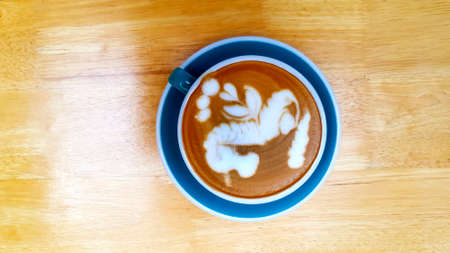 Top view of cup of art cappuccino or latte coffee on wooden background or table at cafÃ© shop. Flat lay of hot drinking in blue glass. Food design concept.の写真素材