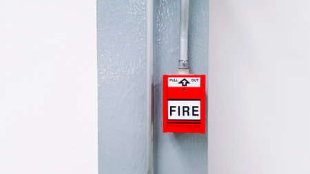 Red fire alarm button for pull out in emergency case happen installed on gray or grey steel pole with white wall background and copy space. Warning equipment or tool.の写真素材