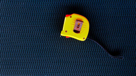 Yellow Tape measure on black conveyor belt background with copy space on left. Tool for