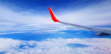 Red and gray or grey wing of plane with blue sky and white cloud background and copy space. Aerial...