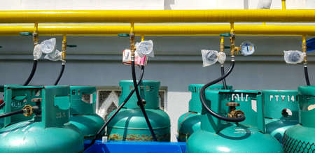 Bangkok, Thailand - March 5, 2022: Group of new green gas tank install with value, yellow pipe or pipeline and white wall background. Object to make fire for cooking food in kitchen.のeditorial素材
