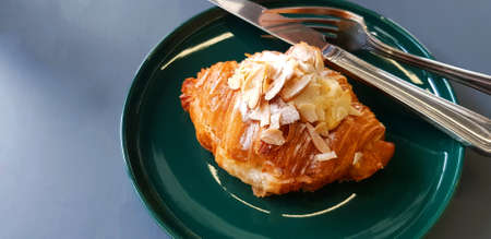 Croissant with icing sugar and almond sliced with stainless steel knife in green dish on gray table...