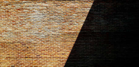 Brown or red brick wall with shadow for background. Art and Pattern wallpaper. Rough and Grunge exterior or interior design with copy spaceの写真素材
