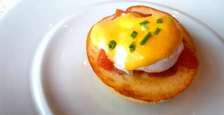 Close up bread with poached egg, bacon and sweet sauce on top in dish. Delicious meal of breakfast on white plate in American style.の写真素材
