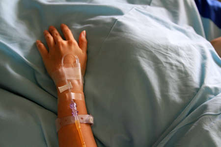 Patient's hands giving the saline solution on bed with copy space. Healthy, Medicine or Medical and injection. People cure sickness and fever at hospital or clinic concept.の写真素材