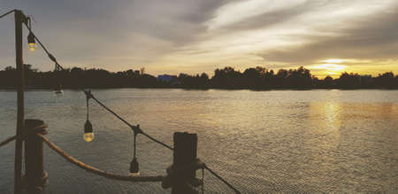 Silhouette of lighting lamp with rope and wide river, sky and tree background at sunset or sunshine time. Beautiful of nature, freshness and freedom. Natural wallpaper with copy spの写真素材