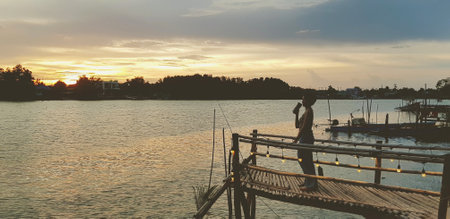 Silhouette of woman stand on wooden waterside, waterfront or bridge with rive and tree background at sunset or sunshine. Beautiful nature. Natural wallpaper with copy space in vintの写真素材
