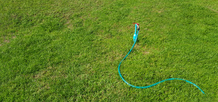 Faucet with hose for watering plants on green grass field or lawn with copy space. Tools for make garden, Natural wallpaper and Beauty of nature.の写真素材