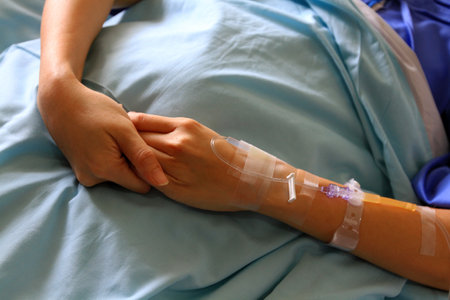 Patient's hands or arm giving the saline solution on bed with copy space. Healthy, Medicine or Medical and injection. People cure sickness and fever at hospital or clinic concept.の写真素材