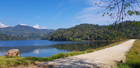 Road or street beside lake or river with green mountain and blue sky background at Huai Bon reservoir Chiang Mai, Thailand. Among nature with reflection on water and copy space. Beの写真素材