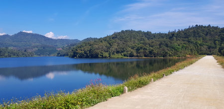 Road or street beside lake or river with green mountain and blue sky background at Huai Bon reservoir Chiang Mai, Thailand. Among nature with reflection on water and copy space. Beの写真素材