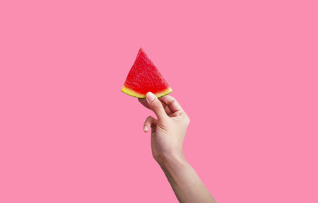 Woman's hand holding sliced piece of fresh watermelon isolated on pink background with clipping path and make selection. Freshness fruit for summertime and Healthy eating food. Delの写真素材