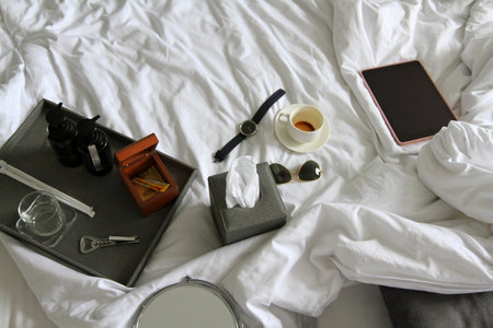 Top view of tablet, watch, black glasses, cup of coffee, gray box of napkin, bottle opener, wooden...