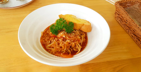 Spaghetti with minced pork, chicken or beef, fried butter bread with sweet tomato sauce in white plate on wooden table. Italian food with parsley on top and delicious meal at lunchtime.の写真素材