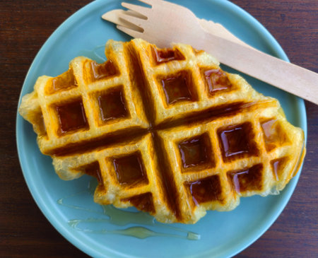 Top view of waffle topped with honey sauce on blue plate at cafe. Flat lay of Sweet bakery on dish...