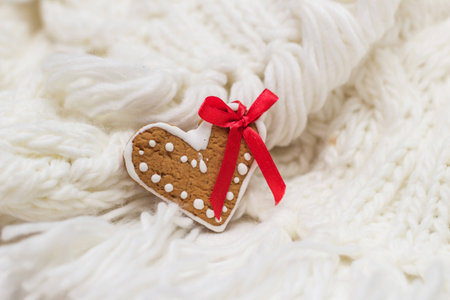 Heart-shaped gingerbread with red ribbon on white knitted clothの写真素材