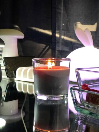 Burning candle, phone chargers, lamp and sweets on glass table in waiting zone of the studioの写真素材