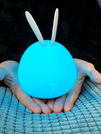 Blue silicon rabbit touch lamp in hands in the darkの写真素材