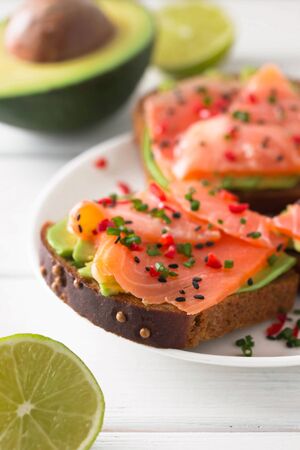 Sandwich with salmon, avocado, sesame, lime and chili pepper on a white wooden background.の写真素材