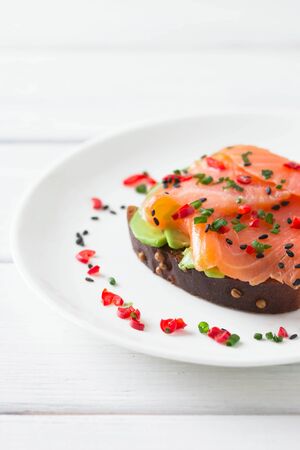 Sandwich with salmon, avocado, sesame, lime and chili pepper on a white wooden background.の写真素材