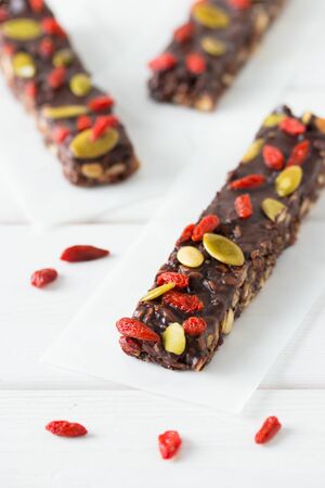 Vegan chocolate bars with granola, nuts, pumpkin and chia seeds. Homemade snack. Super energy bars on a white wooden background.の写真素材