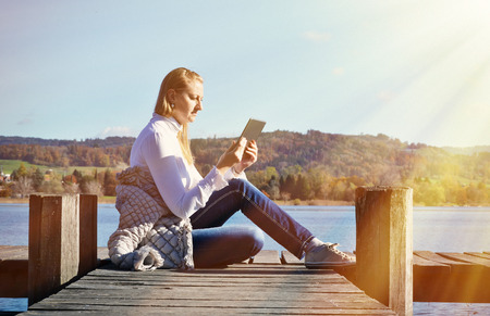 Girl reading from a tablet on the wooden jetty against a lake. Switzerlandの写真素材
